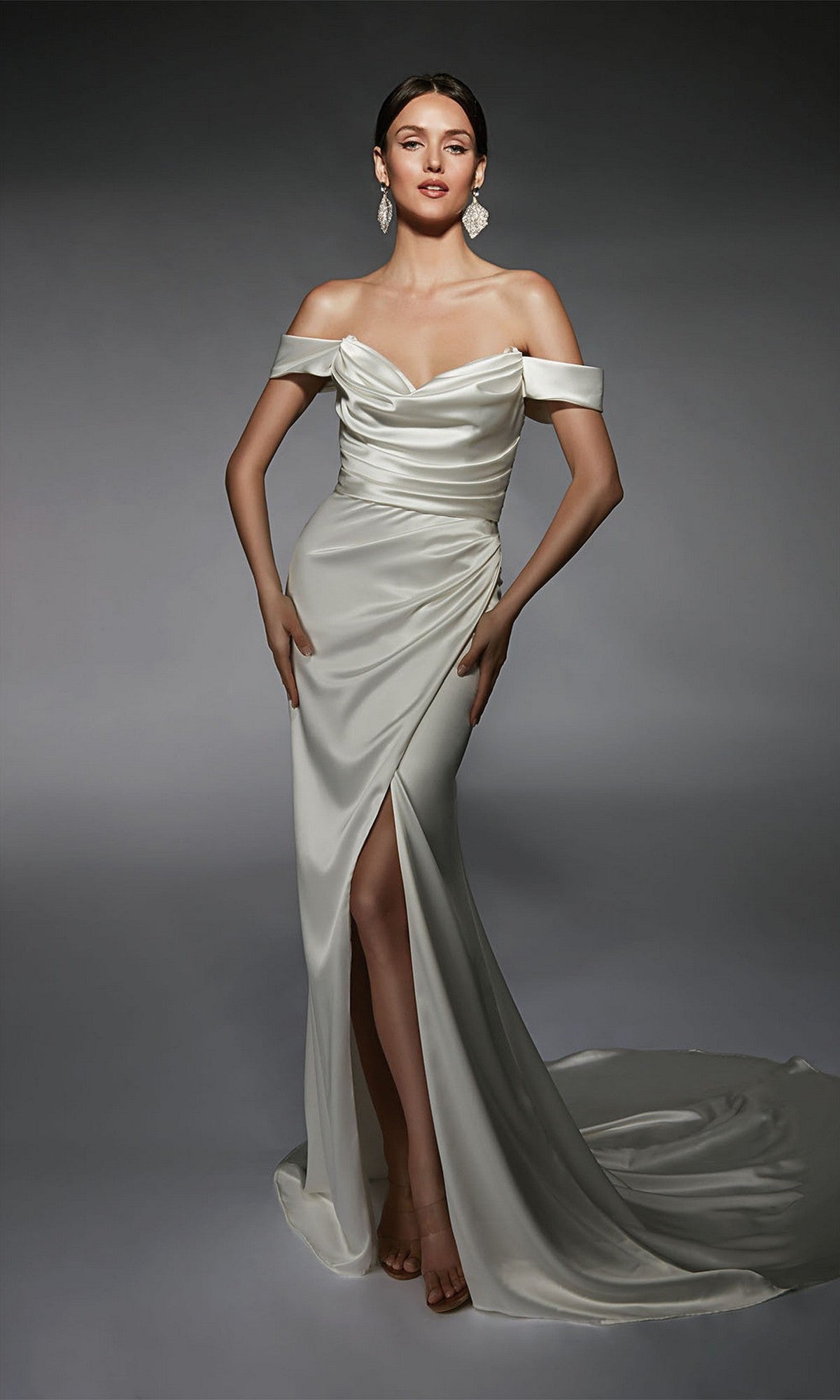 A woman models the Alyce 7106 Long White Dress, featuring a ruched bodice, high slit, train, and detachable overskirt, posing gracefully against a neutral background.